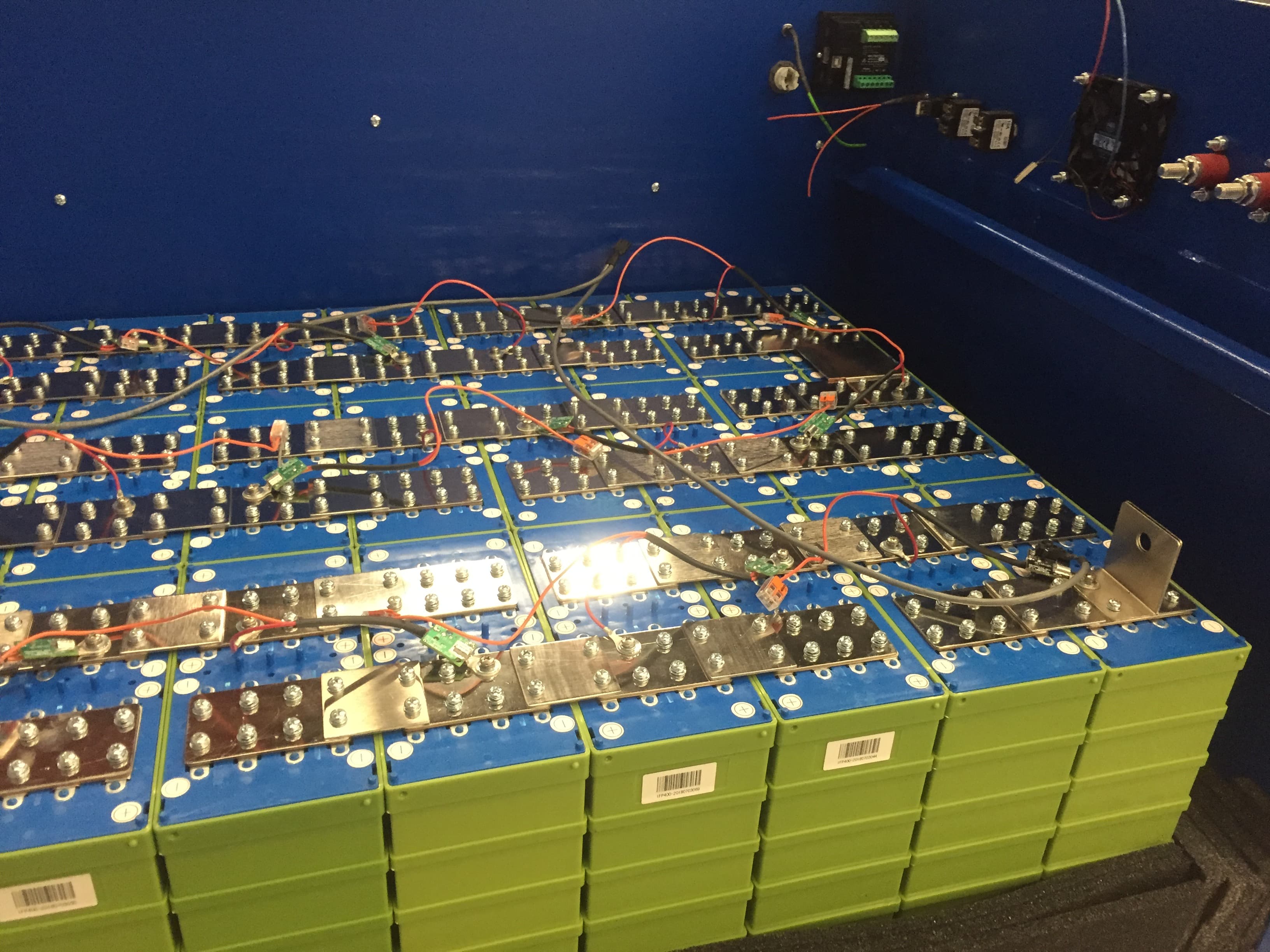 DIY LiFePO4 home battery pack showing green prismatic cells, busbars, and BMS wiring inside a metal enclosure