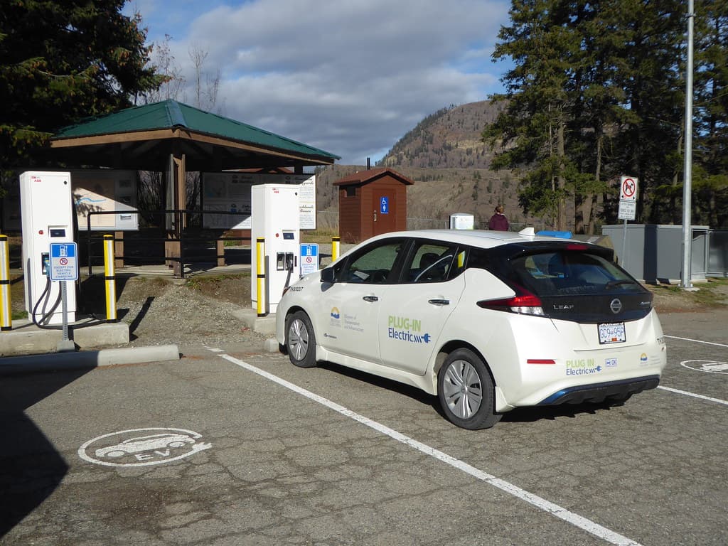 Nissan Leaf charging at a public DCFC station at a highway rest stop in British Columbia, with forested mountains in the background