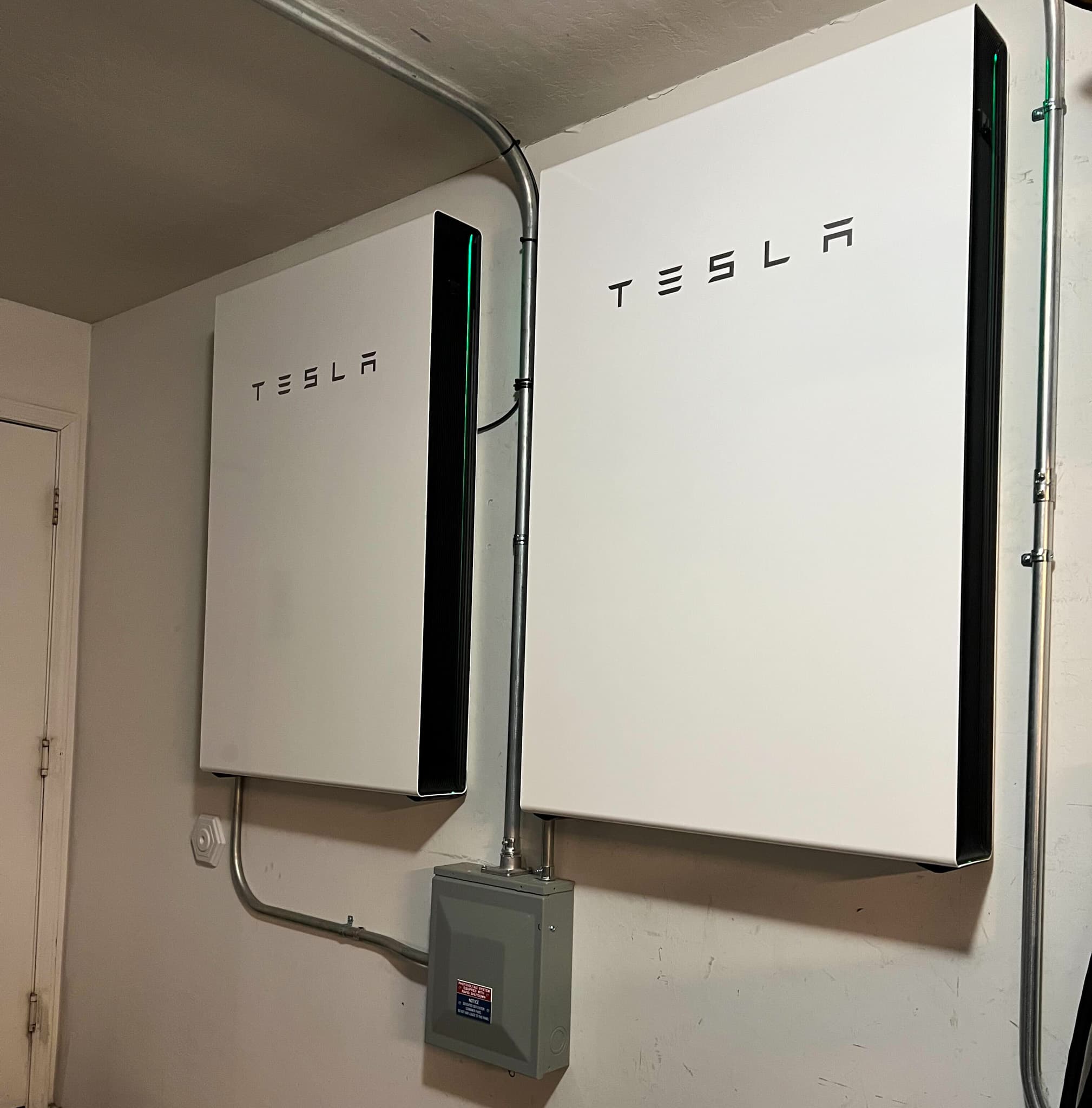 Two Tesla Powerwall 3 units installed on a garage wall with conduit and disconnect box